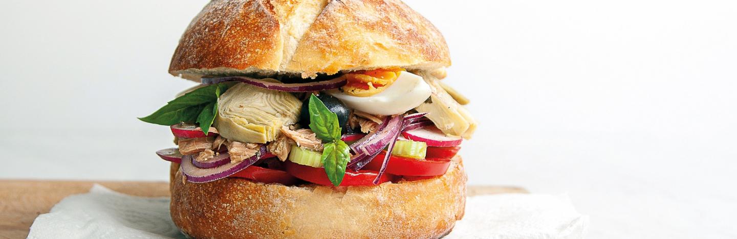 Pan-bagnat sandwich avec pain rond vue de côté, œufs, tomates et thon