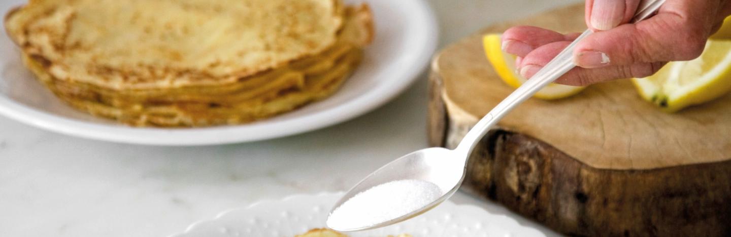 recette de pâte à crêpes - une main met du sucre sur une crêpe dans une assiette recette de pâte à crêpes - une main met du sucre sur une crêpe dans une assiette