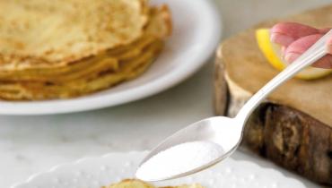 recette de pâte à crêpes - une main met du sucre sur une crêpe dans une assiette