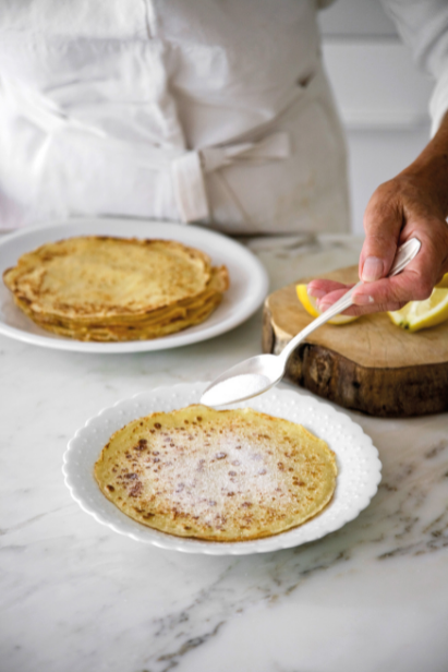 Recette de pâte à crêpes – une main met du sucre sur une crêpe dans une assiette Recette de pâte à crêpes – une main met du sucre sur une crêpe dans une assiette